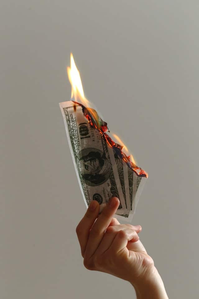 En hand som håller i brinnande dollarsedlar.